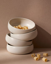Stacked white stoneware tapas bowls with a beige rim, filled with what appears to be pasta. The bowls are set against a neutral background.