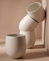 A set of beige stoneware coffee and tea cups with a matte finish, displayed in an artistic manner against a neutral background.