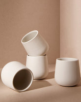 A set of three white stoneware coffee and tea cups of different sizes placed on a textured surface with a neutral background.