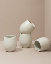 A set of four stoneware coffee cups arranged in a casual manner, with a matte white finish.