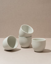 A set of three white stoneware coffee cups of varying sizes placed on a beige surface.