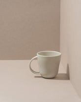 A white stoneware coffee mug placed against a neutral background.