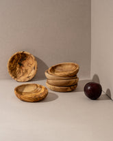 Stacked natural olive wood ramkins on a neutral background, with a shadow falling across the image, highlighting the rustic and handmade aesthetic of the bowls.