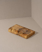 An olive wood soap holder with a natural pattern, placed on a neutral background.