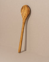 A single round olive wood cooking spoon leaning against a neutral background.