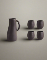 A stoneware jug in green color accompanied by four matching cups, displayed against a neutral background.