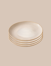 A stack of five round ceramic plates with a warm cream center and a thin gold rim, set against a solid beige background.