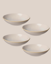 Four white ceramic bowls with a thin gold rim, arranged diagonally on a solid beige background.