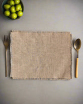 A beige burlap placemat on a gray surface with a fork on the left side and a spoon on the right side, both with wooden handles.