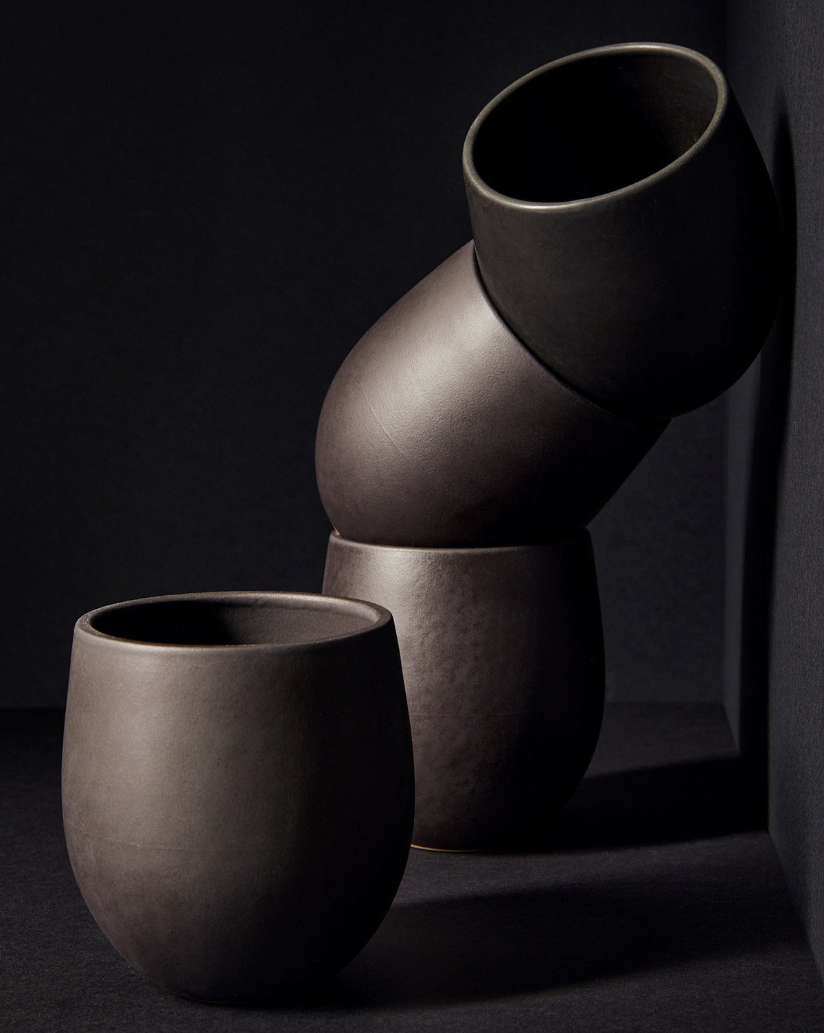 A set of beige stoneware coffee and tea cups with a matte finish, displayed in an artistic manner against a neutral background.