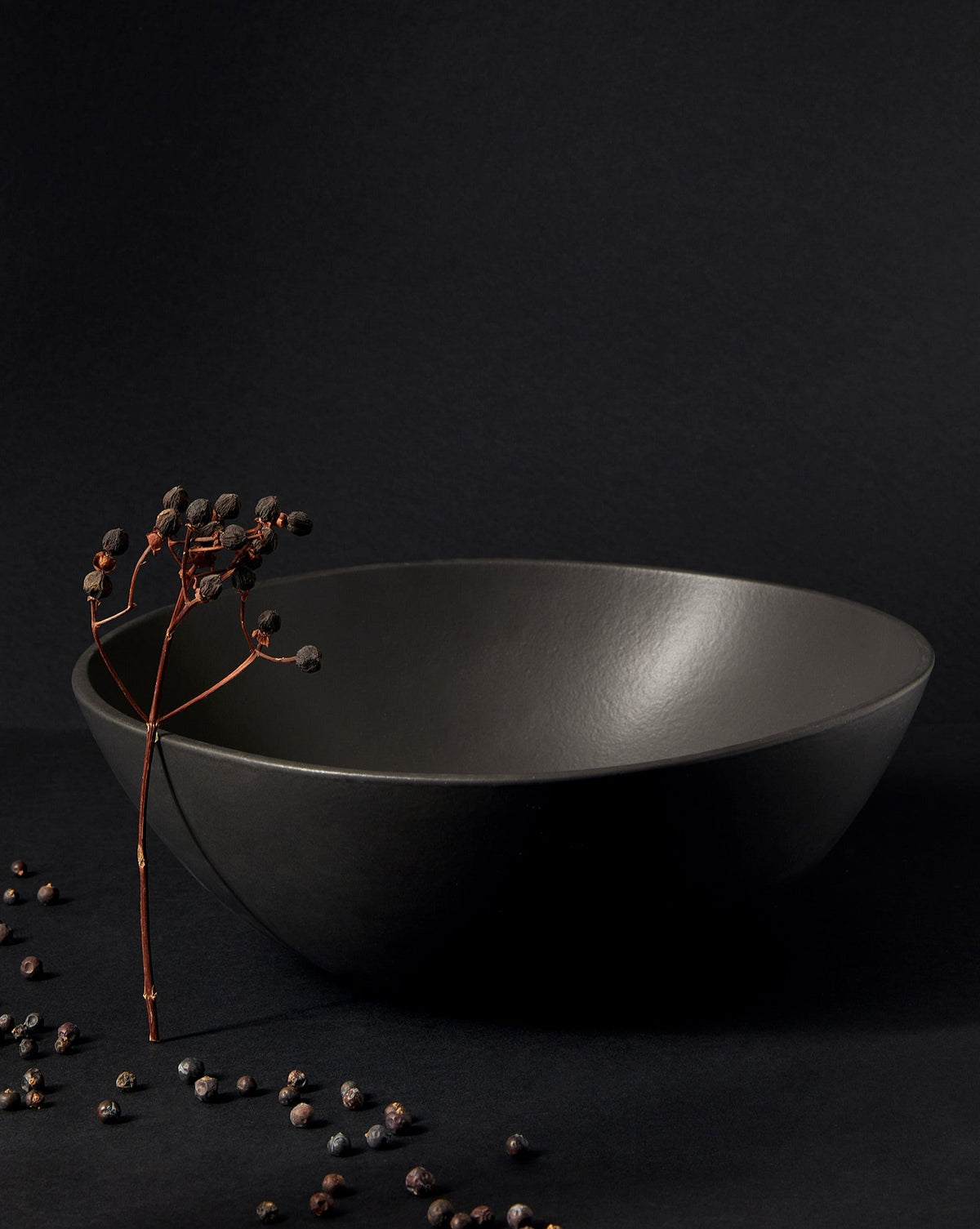 A black stoneware serving bowl with a matte finish on a neutral background, containing what appears to be a few eggs or round items, with the bowl's artisanal craftsmanship highlighted.