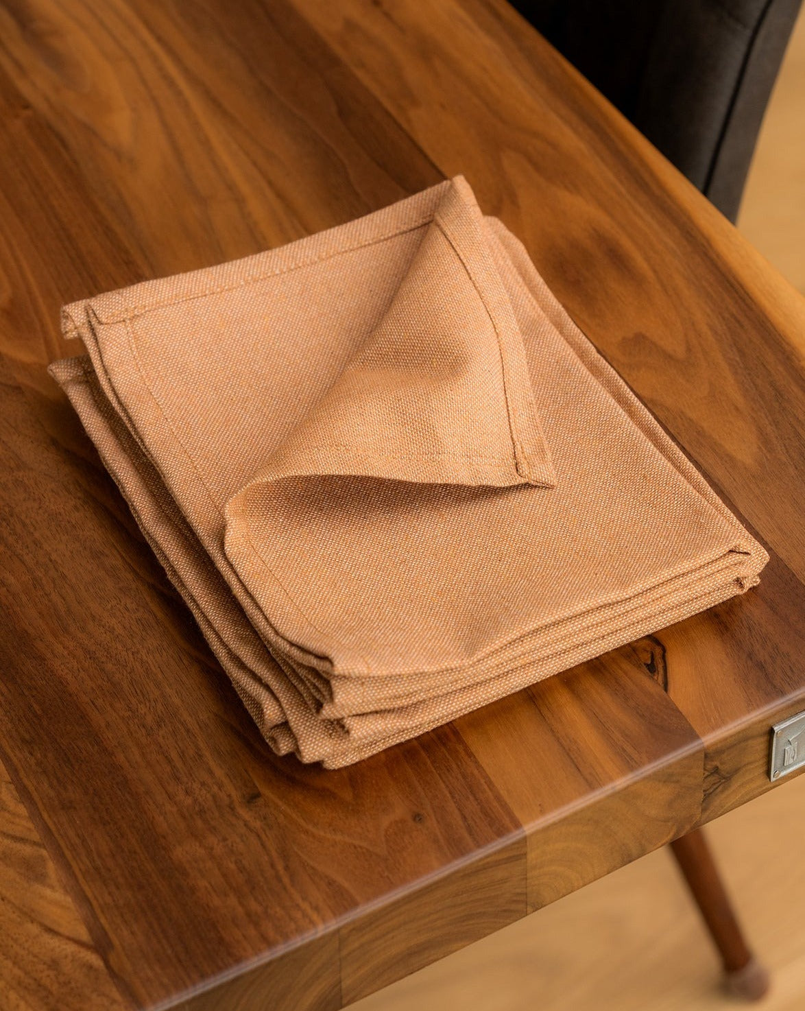 A folded Copper cotton napkin on a wooden dining table