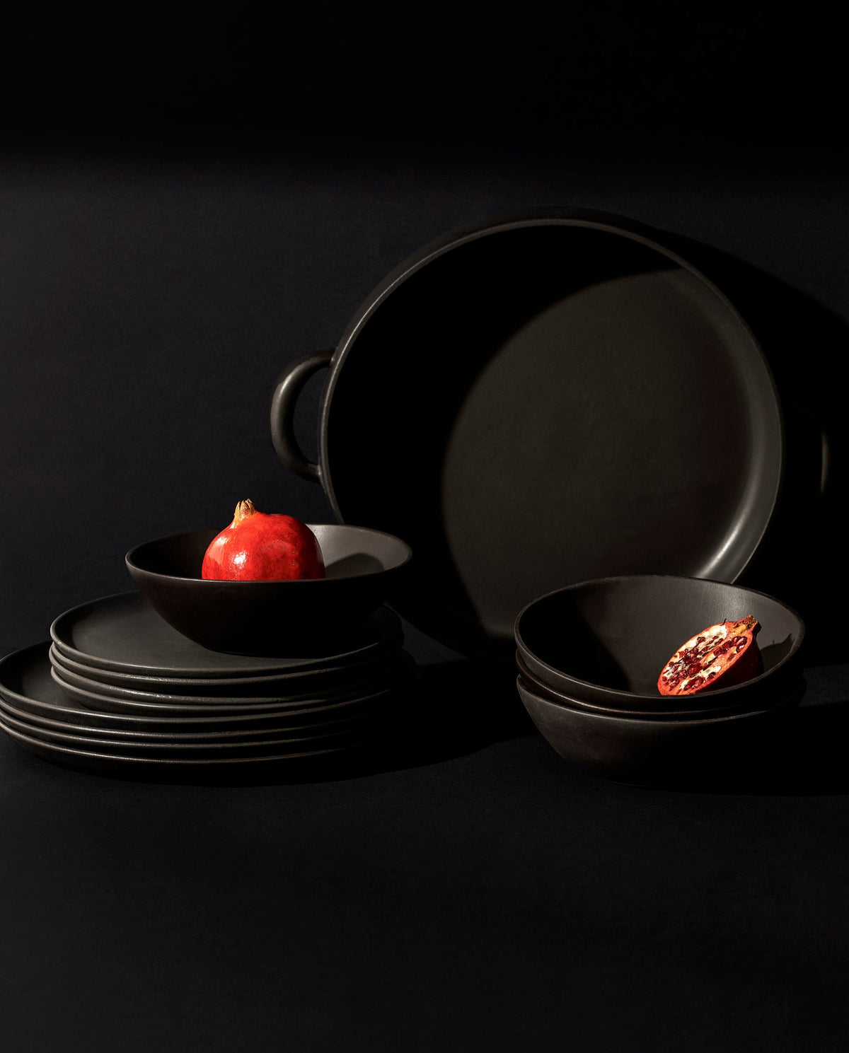 A set of white stoneware dinnerware including flat round dinner plates, flat round salad plates, organic-shaped soup bowls, and a large plate with handles.