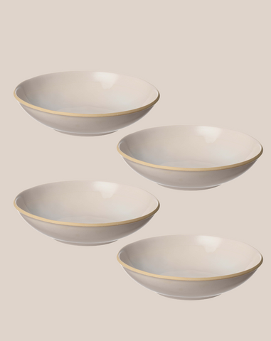 Four white ceramic bowls with a thin gold rim, arranged diagonally on a solid beige background.