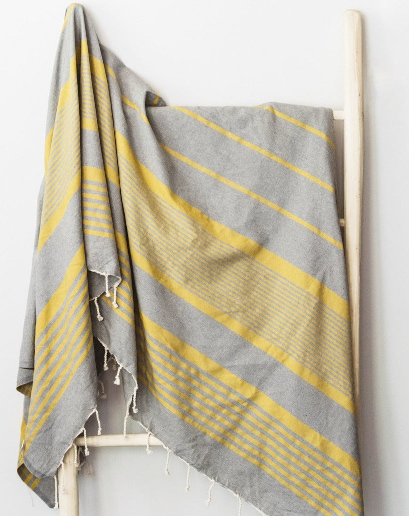 A yellow/ grey cotton throw blanket draped over a wooden rack, with part of the blanket visible on the ground.